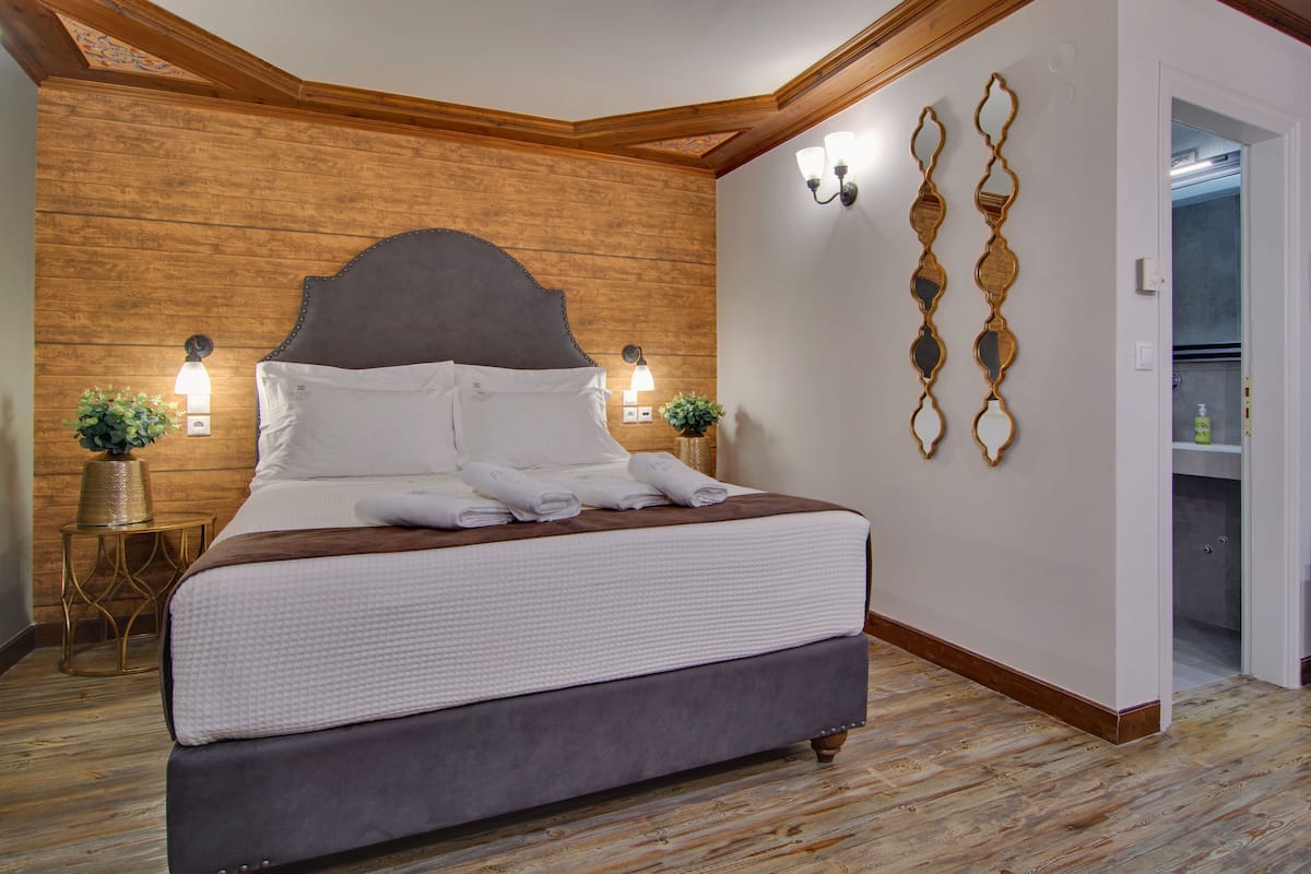 A neatly made bed with a grey headboard, two wall-mounted lights, and a wooden accent wall.