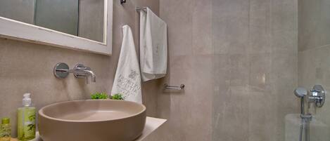 A bathroom with a large beige sink, a glass shower enclosure, and a towel rack with a white towel.