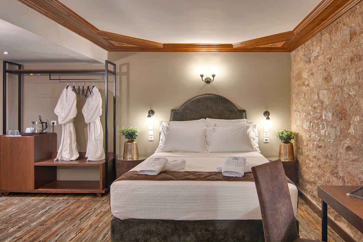 A hotel room with a large bed, bedside tables, a robe rack, and a stone wall.