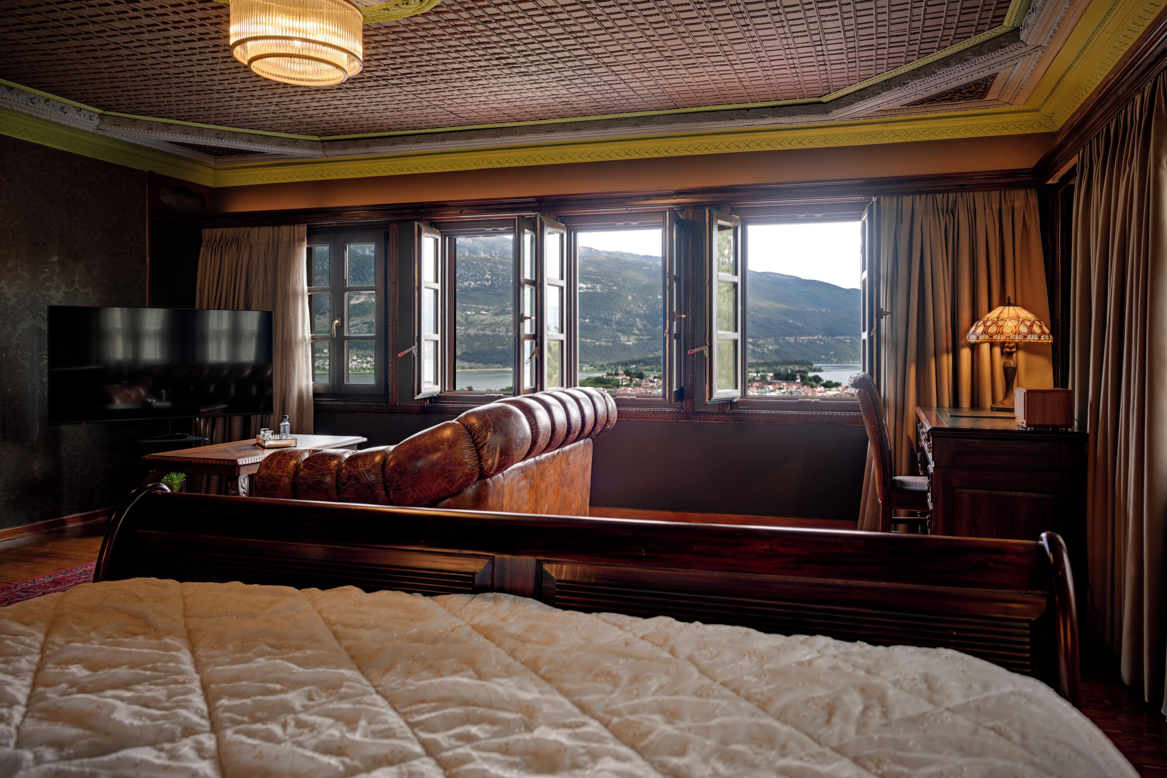 Habitación de hotel con una cama grande, televisión, sofá y vistas a las montañas a través de las ventanas.