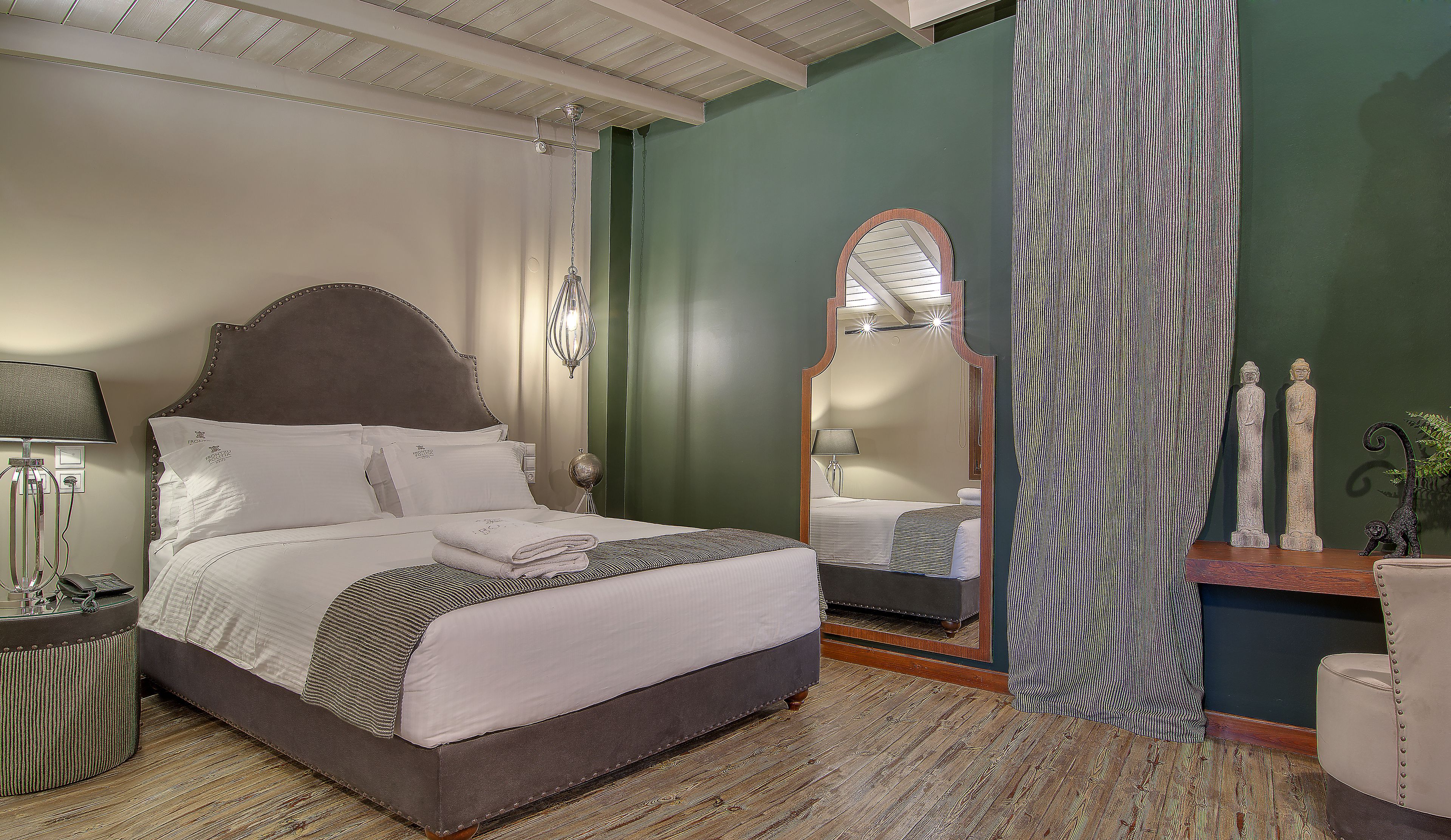 A neatly made bed with a headboard, a bedside lamp, a mirror, and a small statue on a nightstand.