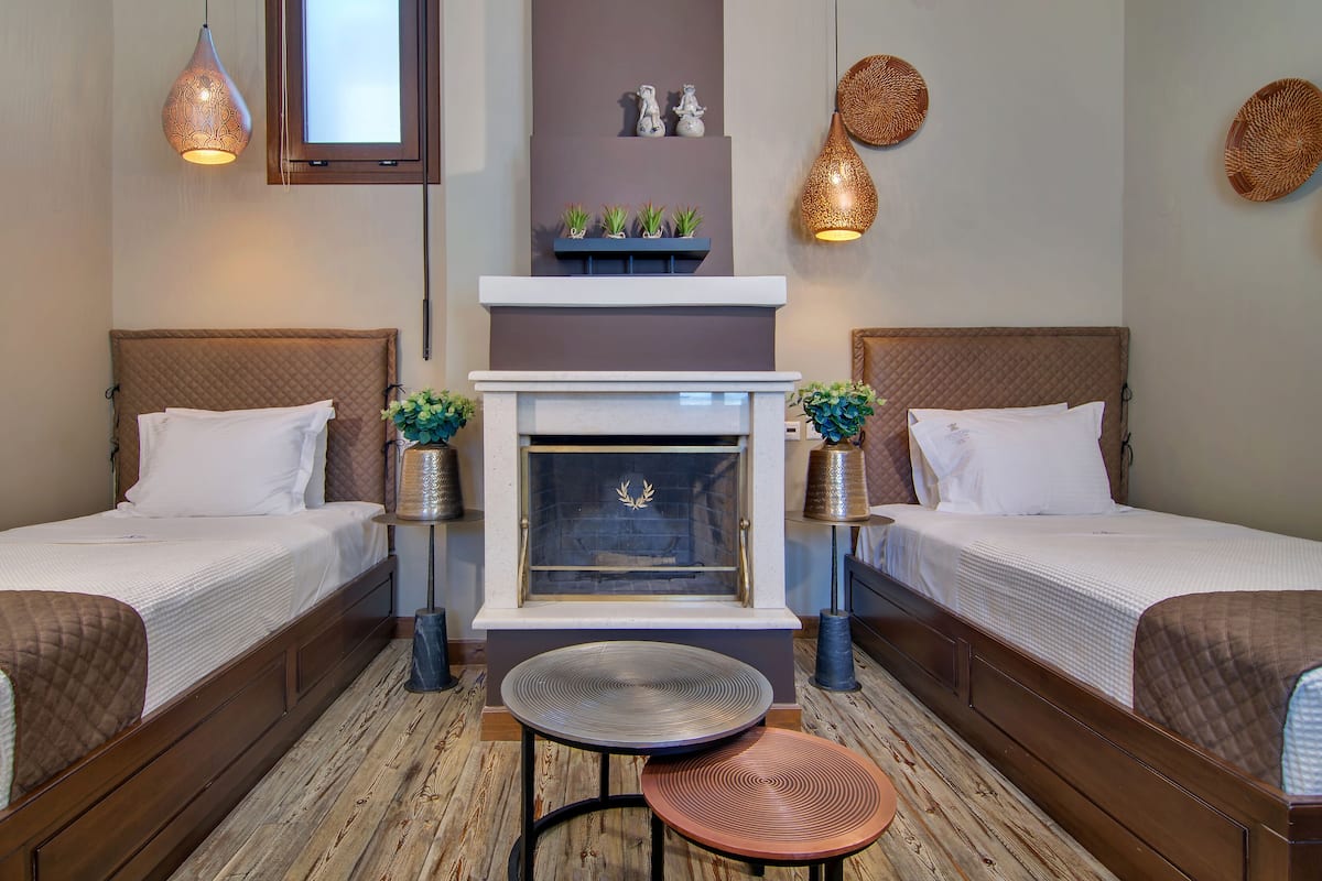 A hotel room with two single beds, a small table, a fireplace, and decorative wall art.