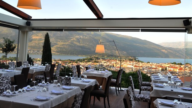 An outdoor dining area with tables set for two, overlooking a scenic view of a lake and mountains. - Frontzu Politia (Ioannina)
