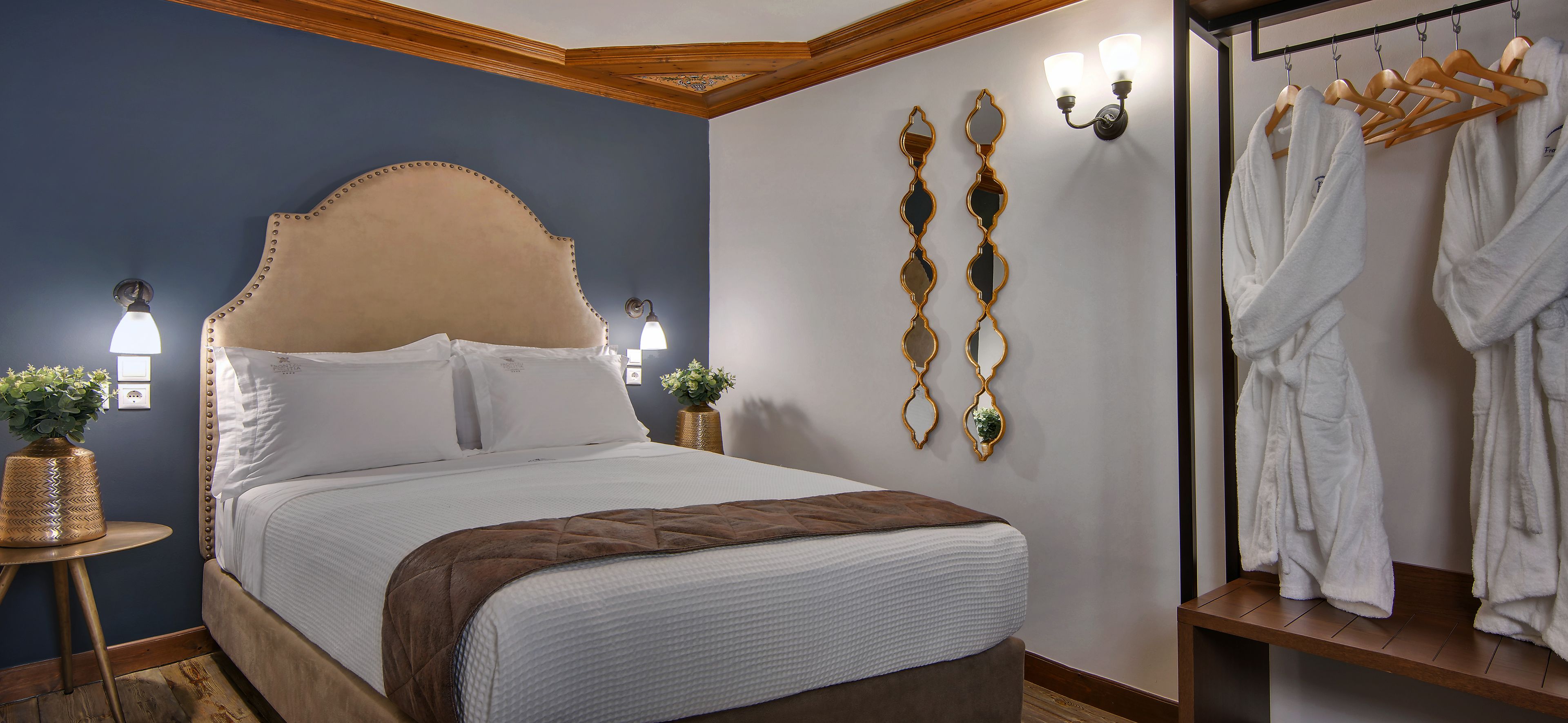 A neatly made bed with a headboard, bedside tables with lamps, and a wall-mounted robe rack.