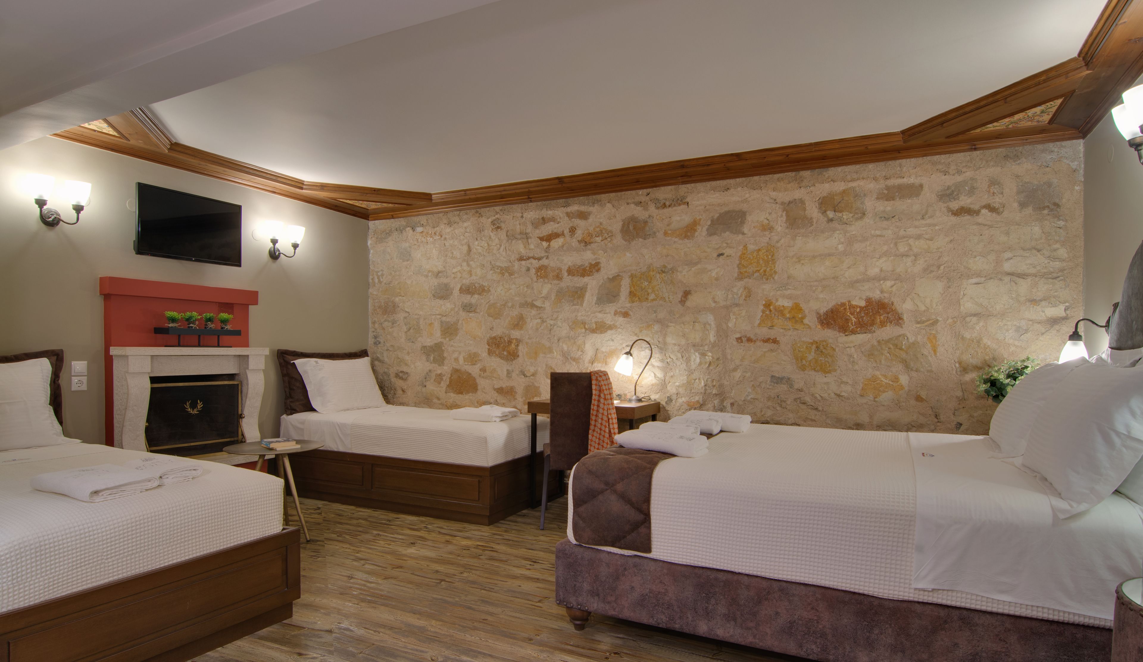A hotel room with two beds, a fireplace, stone walls, and a flat-screen TV.
