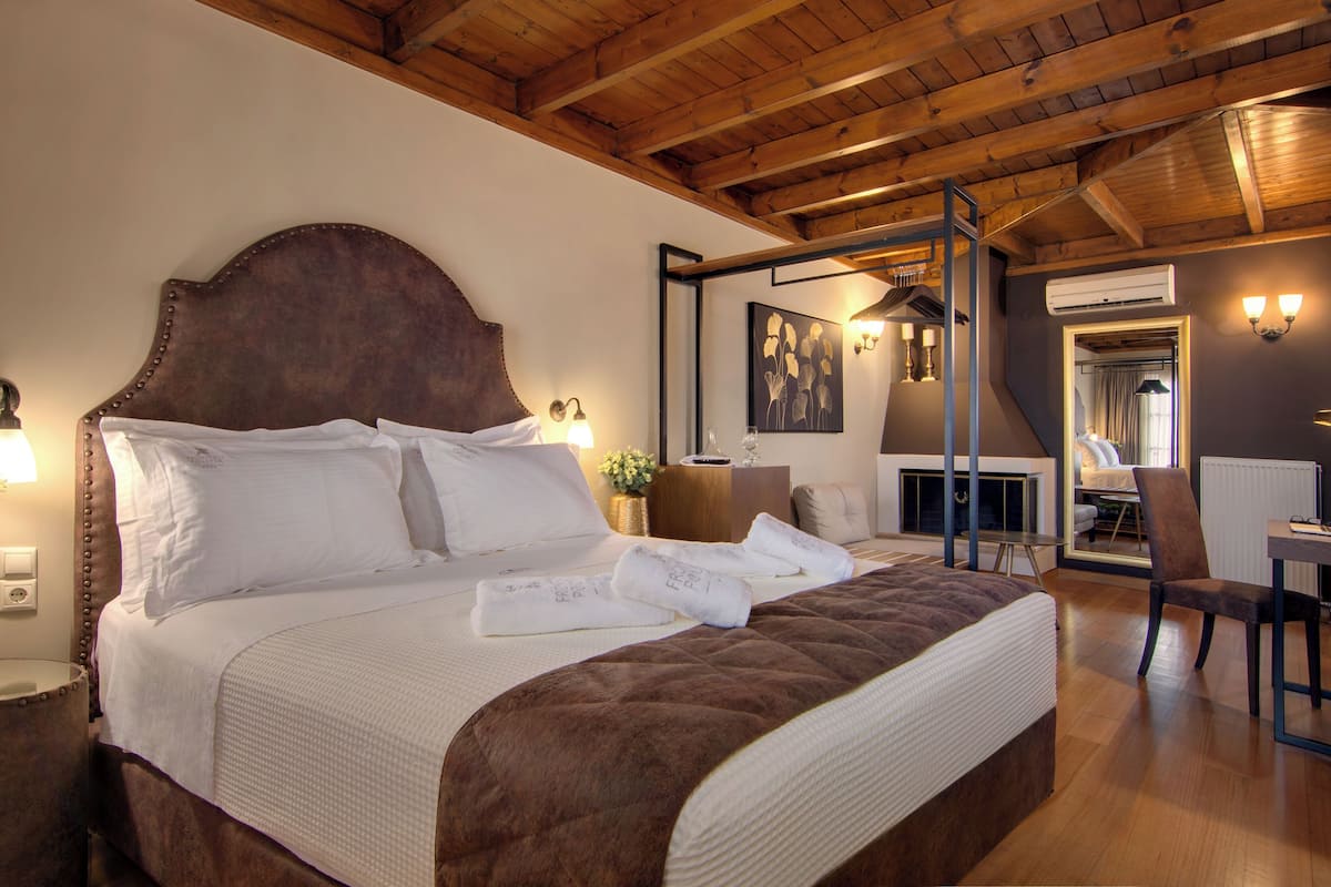A neatly made bed with white linens and a brown headboard, a bedside table with a lamp, and a mirror reflecting the room.