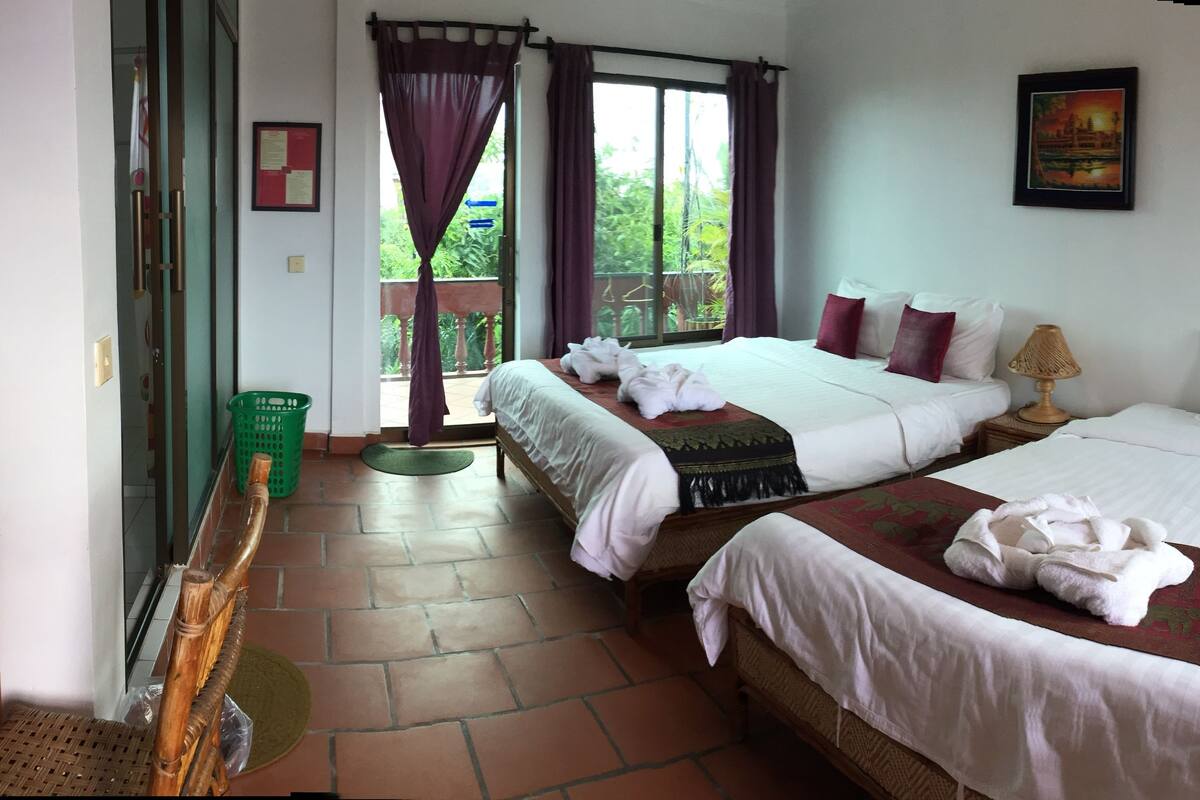 Ein Hotelzimmer mit zwei Betten, einer Sitzecke mit Korbmöbeln, einer grünen Matte und Blick ins Grüne.