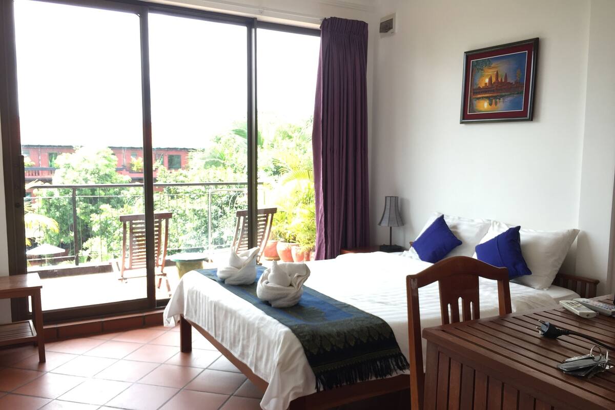 Ein Hotelzimmer mit Bett, Schreibtisch, Stuhl, Tisch, Lampe und Blick ins Freie.