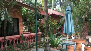 A courtyard with a brick building, a blue umbrella, terracotta planters, and a decorative lamp. - L'Elephant Blanc Resort (Phnom Penh)