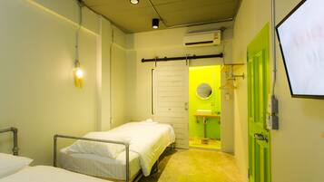 Una habitación pequeña e iluminada con una cama, una mesita de noche y una puerta verde que da al baño.