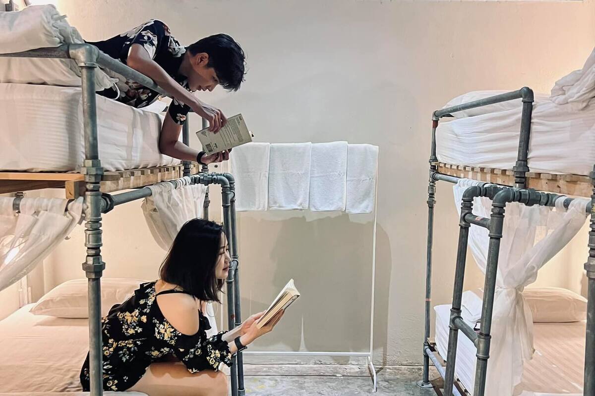A dormitory room with bunk beds, a small table with a white cloth, and an air conditioning unit above the windows.