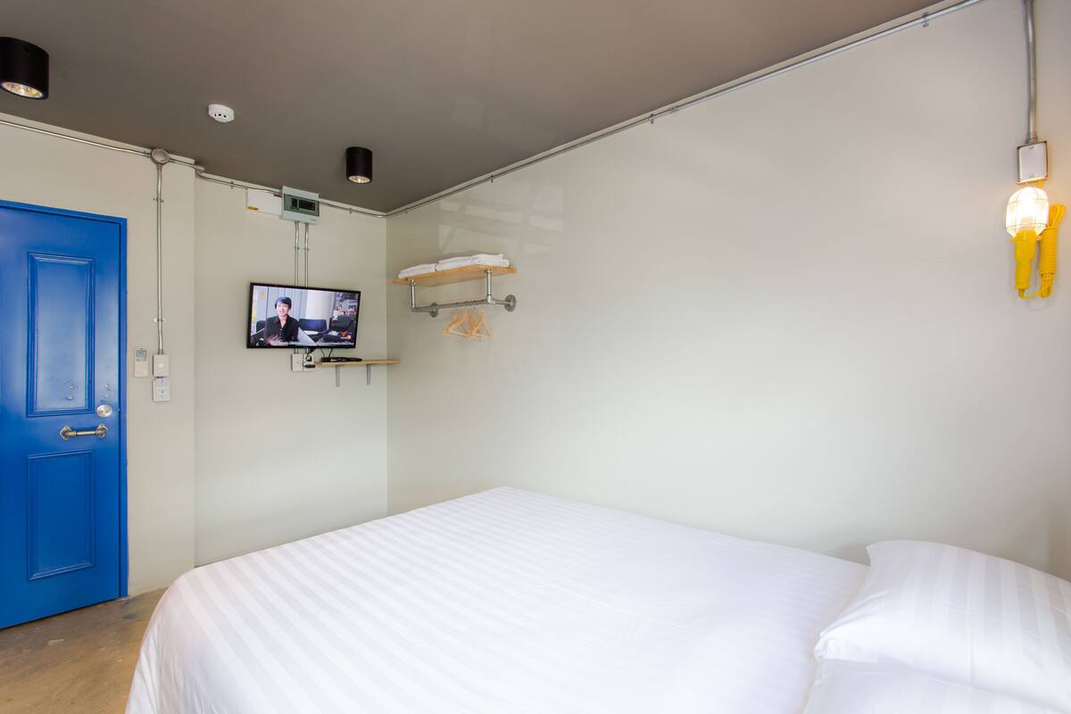 A hotel room with a large bed, a blue door, a television mounted on the wall, and a towel rack.