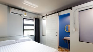 Una camera d'albergo con un letto, una finestra con tende, una porta bianca e un bagno con lavandino e specchio.