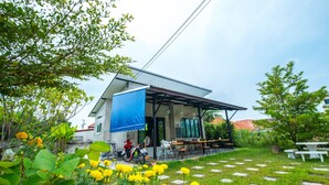 A building with a covered patio area, outdoor seating, and a garden with yellow flowers. - Sweet Dreams Guest House (Phetchaburi)