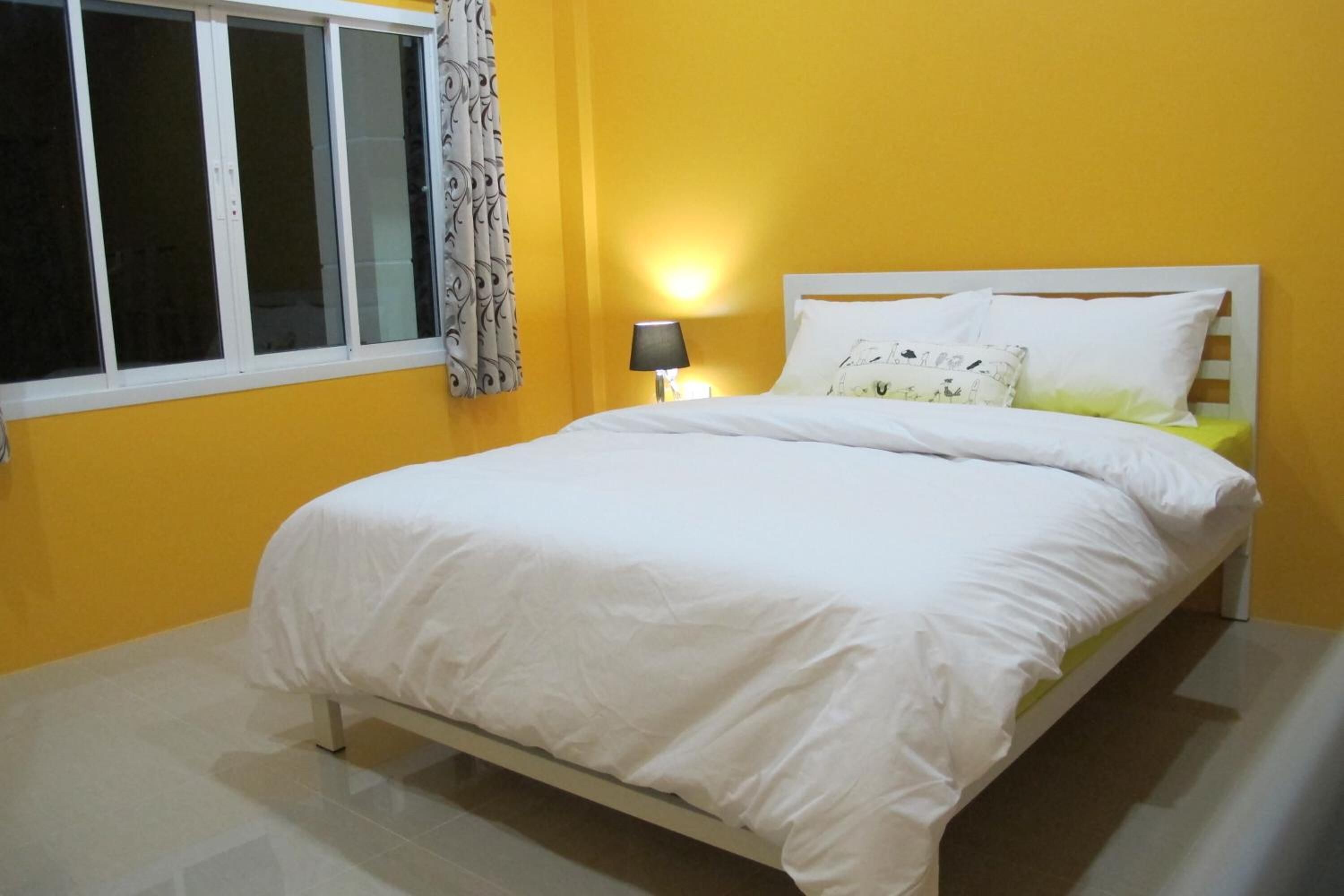 Une chambre à coucher avec un lit, une table de chevet, une lampe et une fenêtre avec des rideaux.