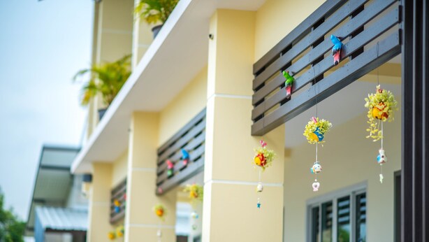 A building facade with balconies, decorative hanging ornaments, and a window with blinds. - Sweet Dreams Guest House (Phetchaburi)