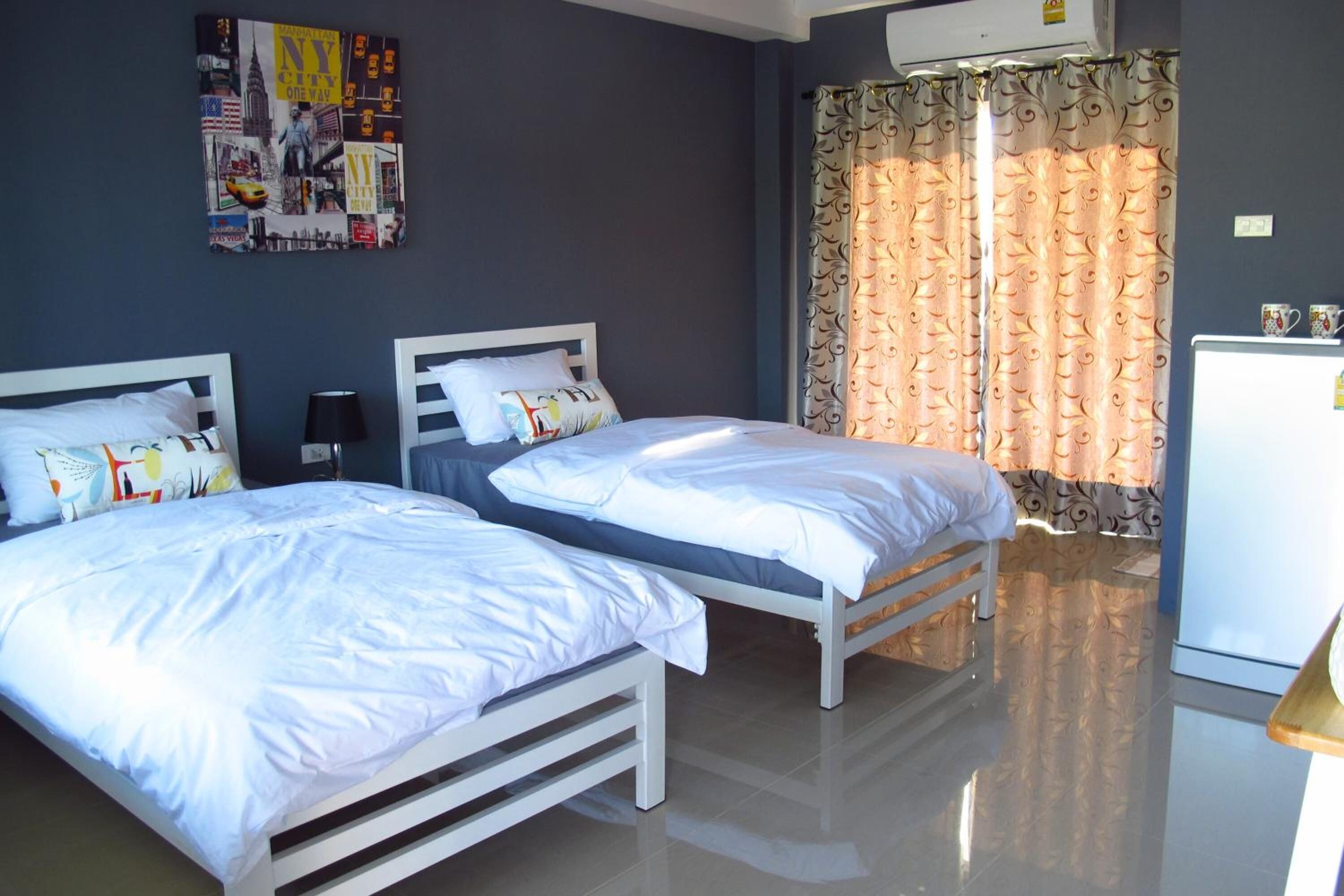 Habitación de hotel con dos camas individuales, un refrigerador pequeño y una pared decorada con un póster de un paisaje urbano.