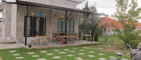 A building with a patio area featuring tables and chairs, a bicycle, and a well-maintained lawn with stepping stones.