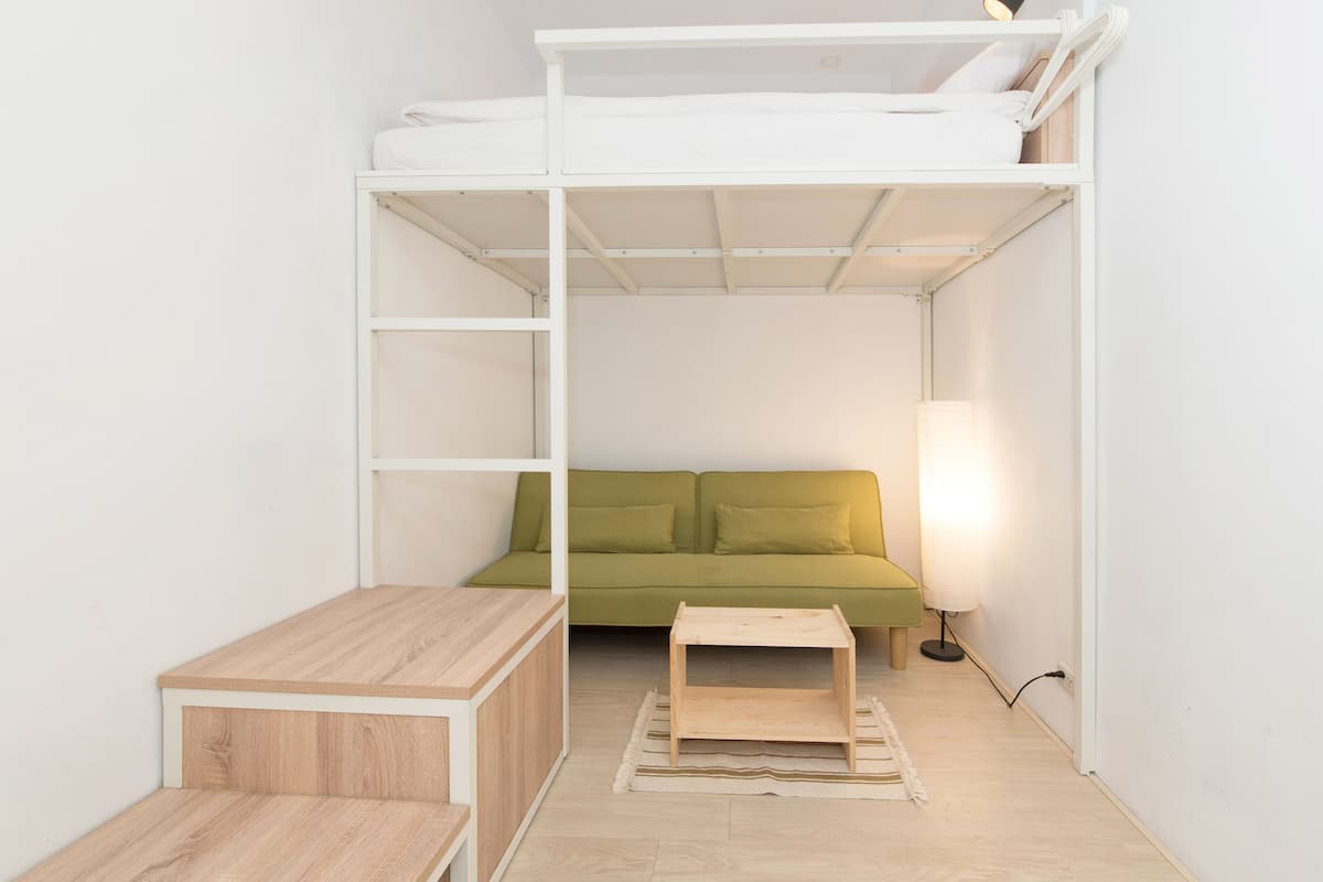 Une pièce de taille modeste, équipée d’un lit superposé, d’un canapé vert et d’une petite table en bois.