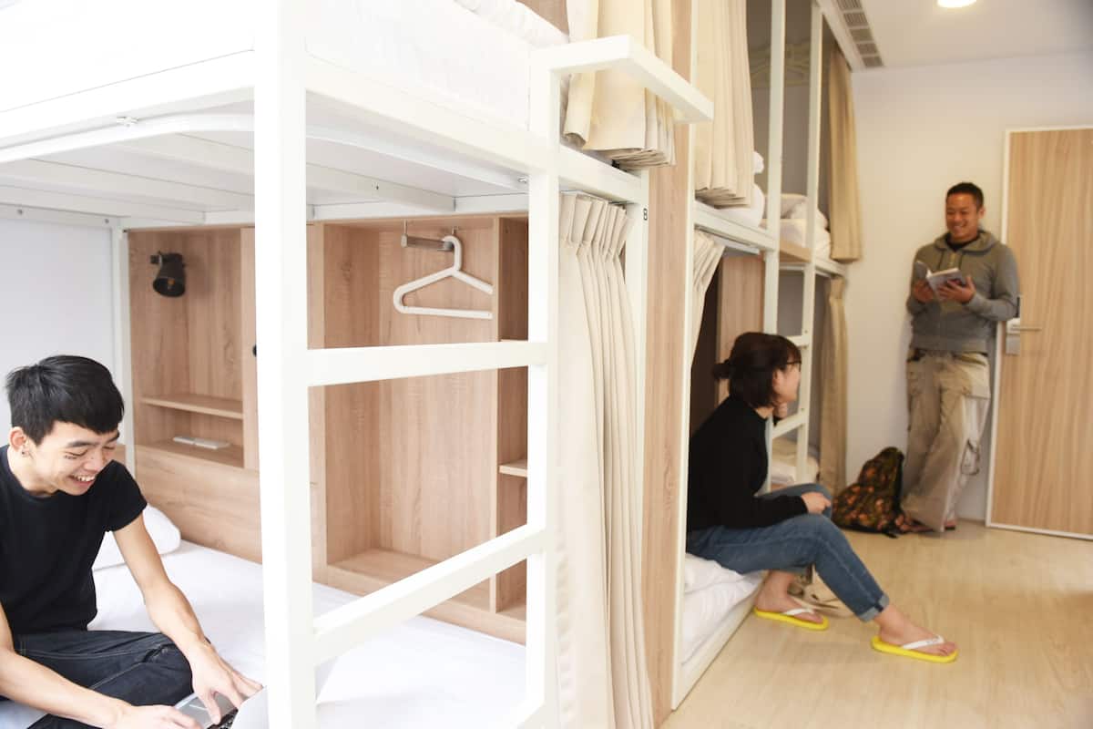 Une chambre de type dortoir, avec des lits superposés, une armoire en bois et un portant à vêtements.