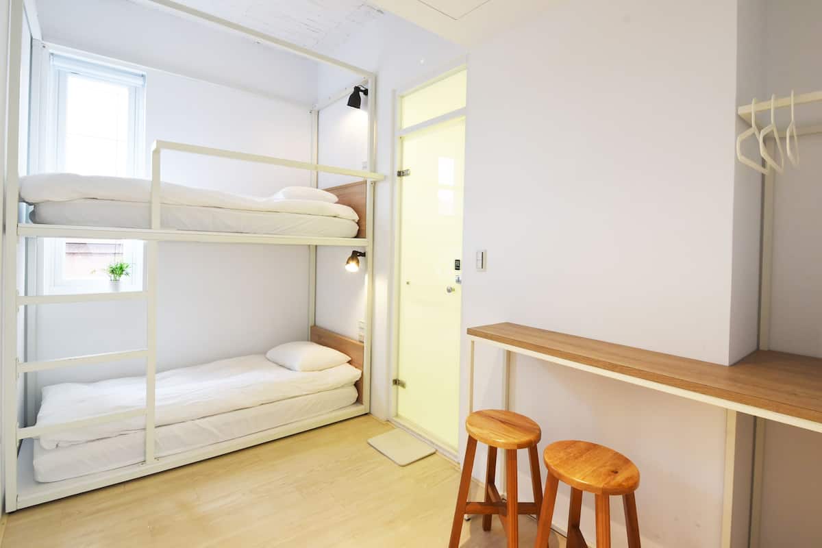 Une petite pièce comprenant un lit superposé, un petit tabouret et une table en bois.