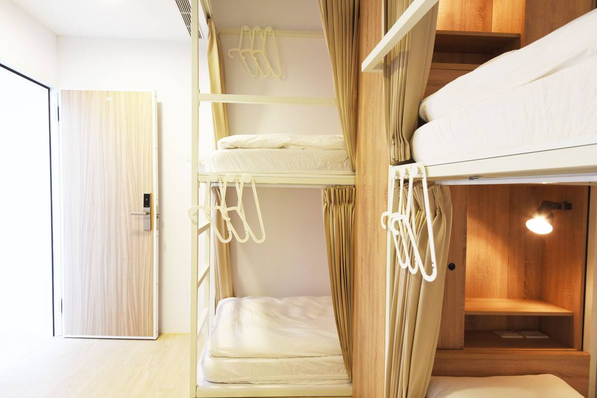 Une chambre avec un lit superposé, une porte en bois, une petite étagère et un luminaire.