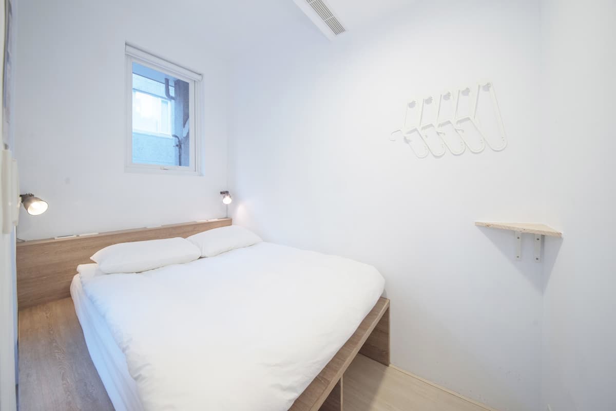 Une chambre à coucher au style minimaliste, avec un cadre de lit en bois, une petite fenêtre et une étagère fixée au mur.