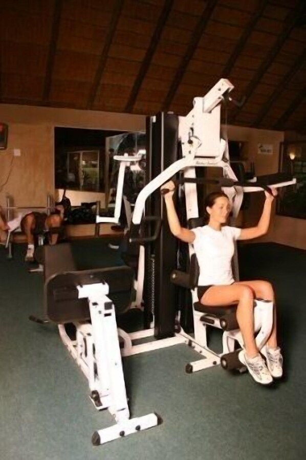 Una persona usando una máquina de prensa de piernas en un gimnasio con techo de madera y una ventana al fondo.