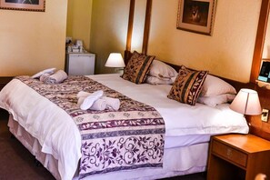 A hotel room with a large bed, two bedside tables, a desk, a lamp, a small refrigerator, and a framed picture on the wall. - Sparkling Waters Hotel & Spa (Rustenburg)
