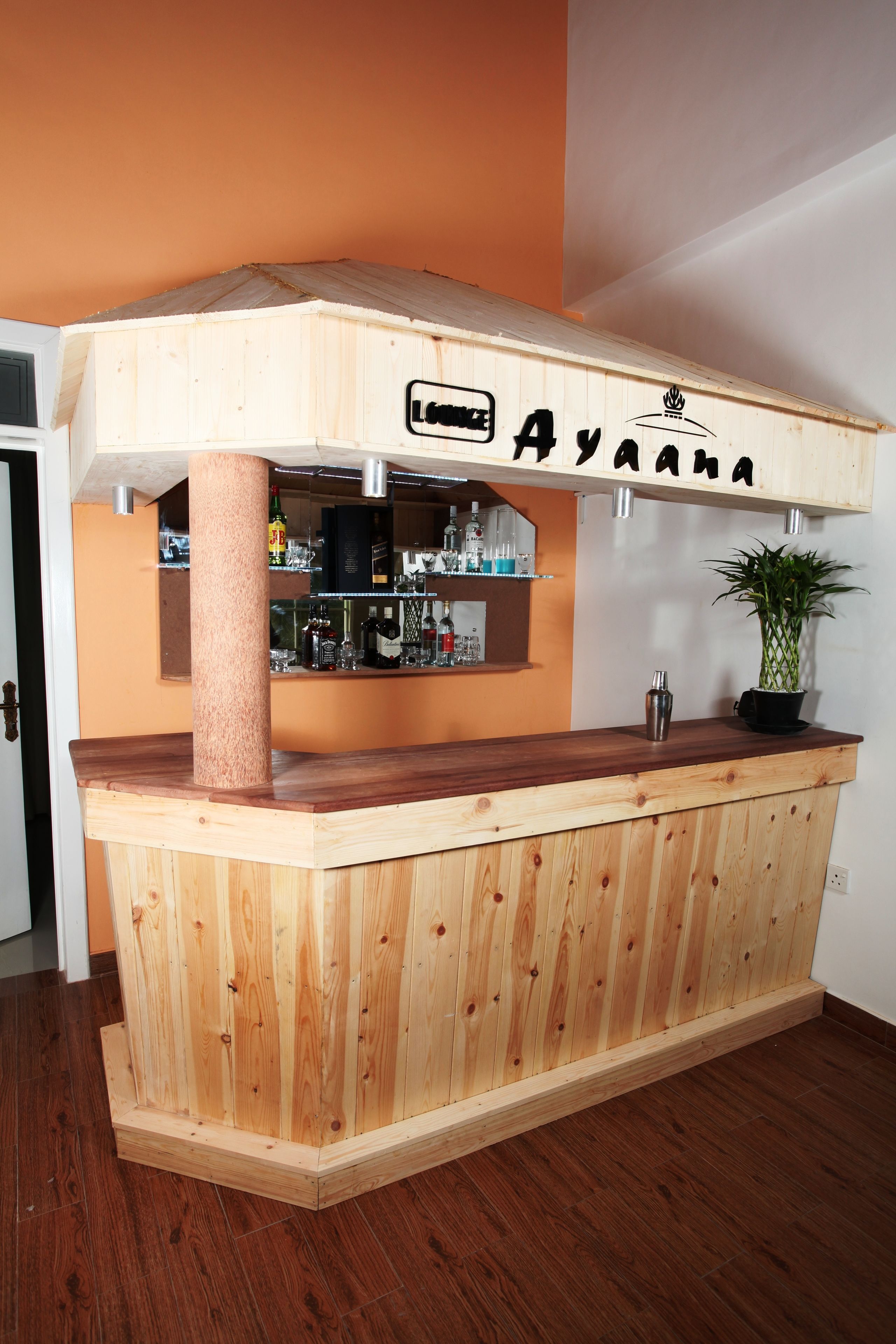 Una zona de bar con barra de madera, un cartel que dice 'Ayanana' y una planta en maceta sobre la encimera.