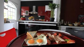Un plateau de petit-déjeuner avec des œufs, des saucisses et des toasts, posé sur une table dans une cuisine moderne aux armoires rouges et à la grande fenêtre.