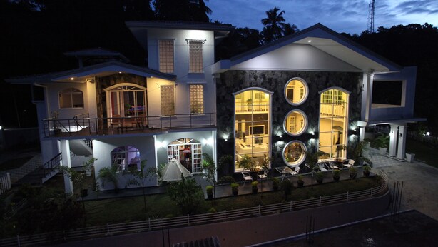 Une maison moderne à deux étages, dotée d’un balcon, de grandes fenêtres et d’un espace extérieur bien éclairé.