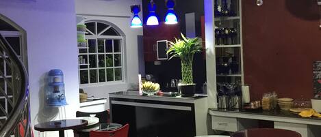 A restaurant interior with a bar area, red chairs, a water dispenser, and a potted plant.