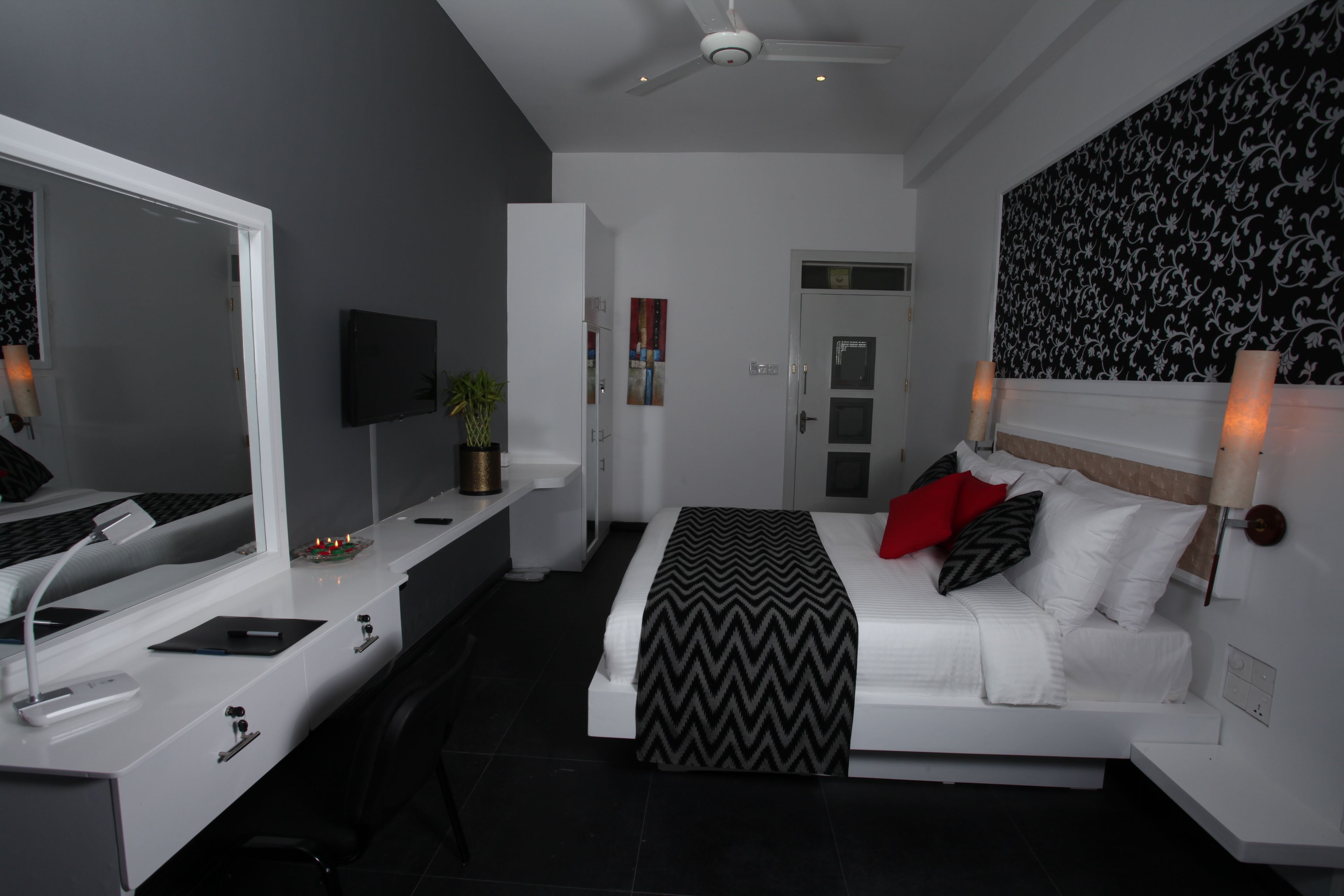 A modern bedroom with a bed, bedside table, desk, and a large mirror.