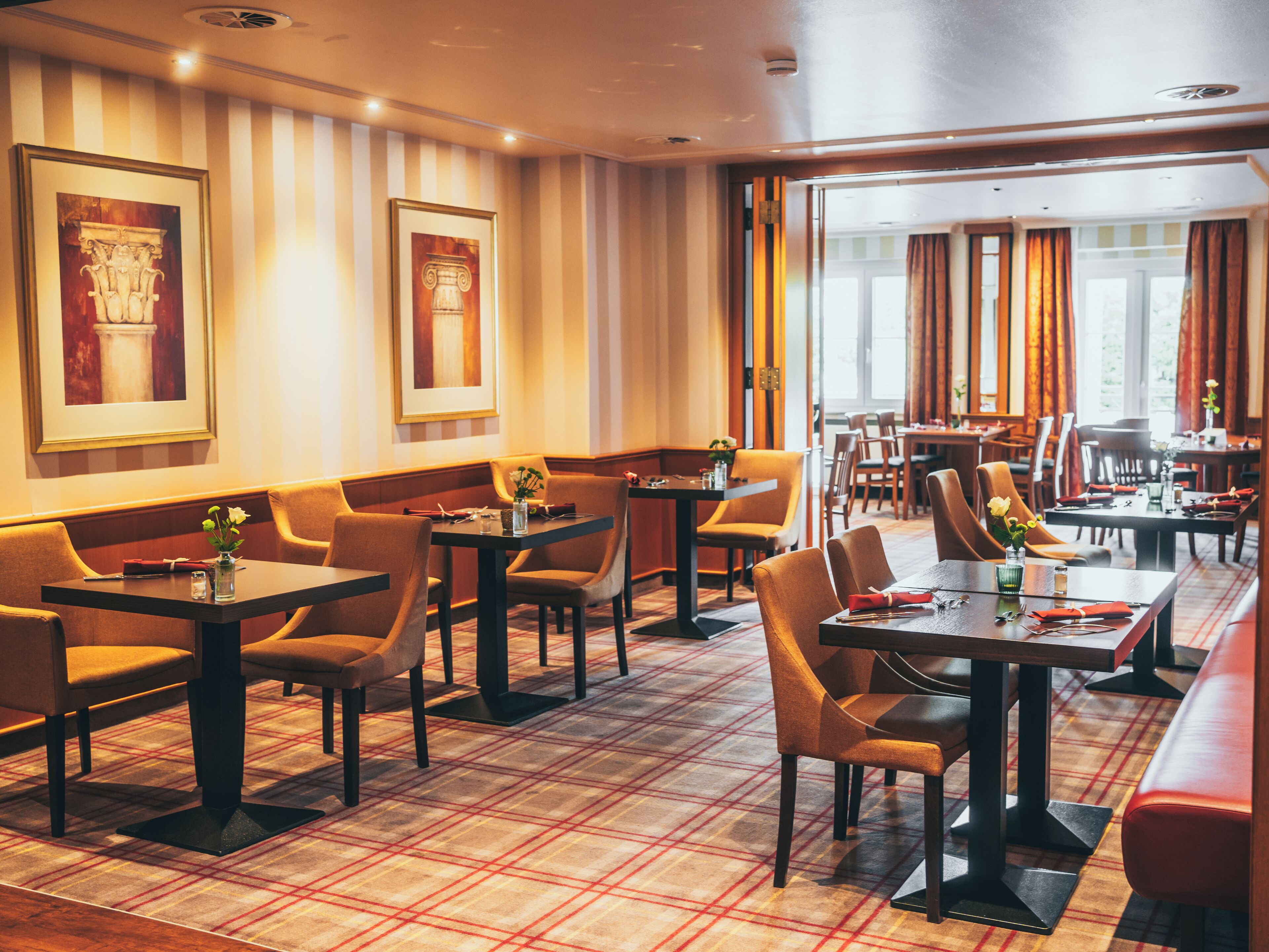 A hotel dining area with tables and chairs, framed artwork on the walls, and a checkered floor pattern.