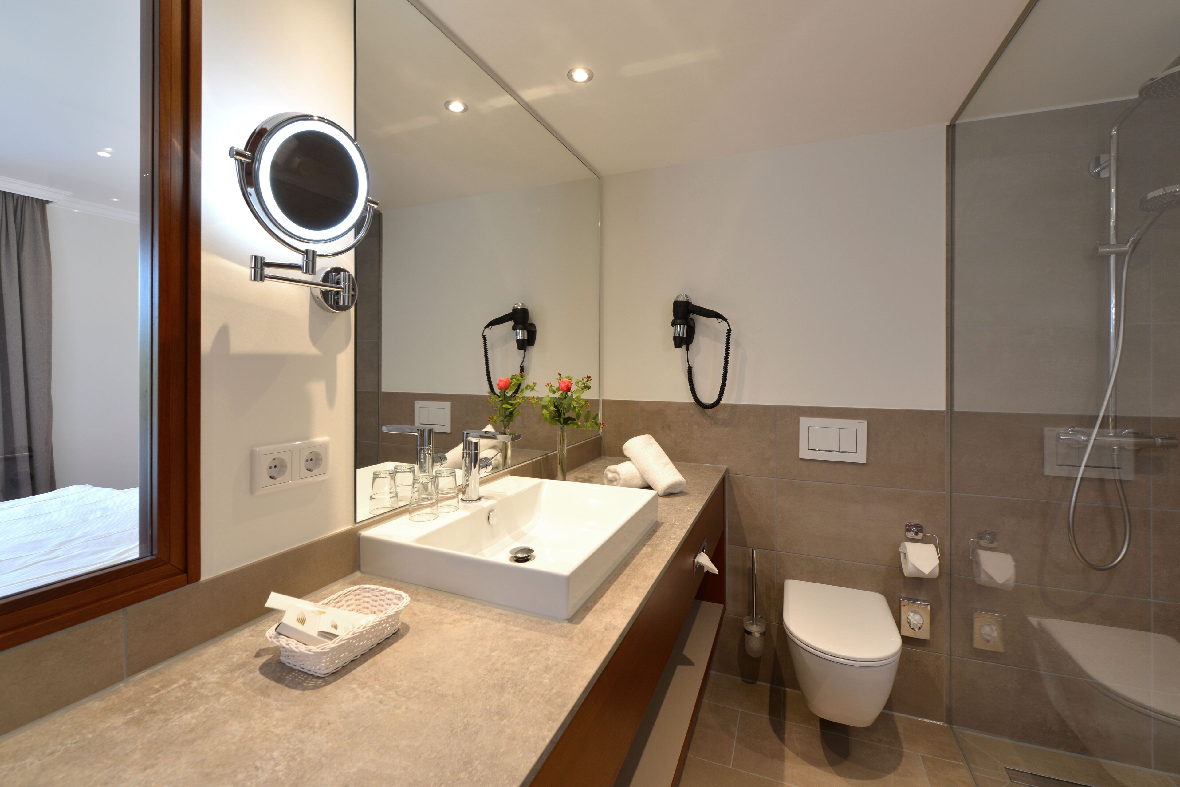 A modern bathroom with a large mirror, a sink, a toilet, and a shower.