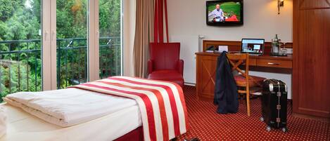 A hotel room with a bed, a desk with a laptop, a chair, a suitcase, and a TV on the wall.