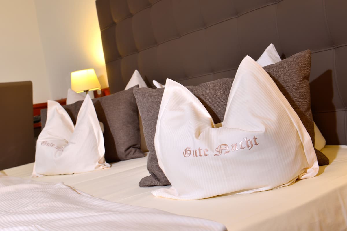 Quarto de hotel com almofadas bem arrumadas na cama, cabeceira e abajur na mesa de cabeceira.