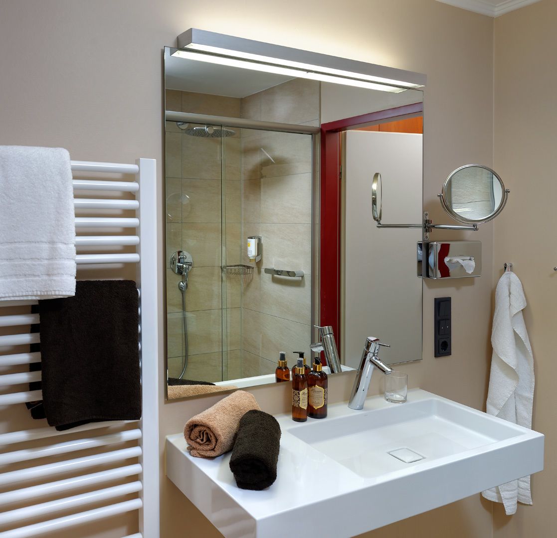A modern bathroom with a large mirror, a glass-enclosed shower, a white sink, and a towel rack with multiple towels.