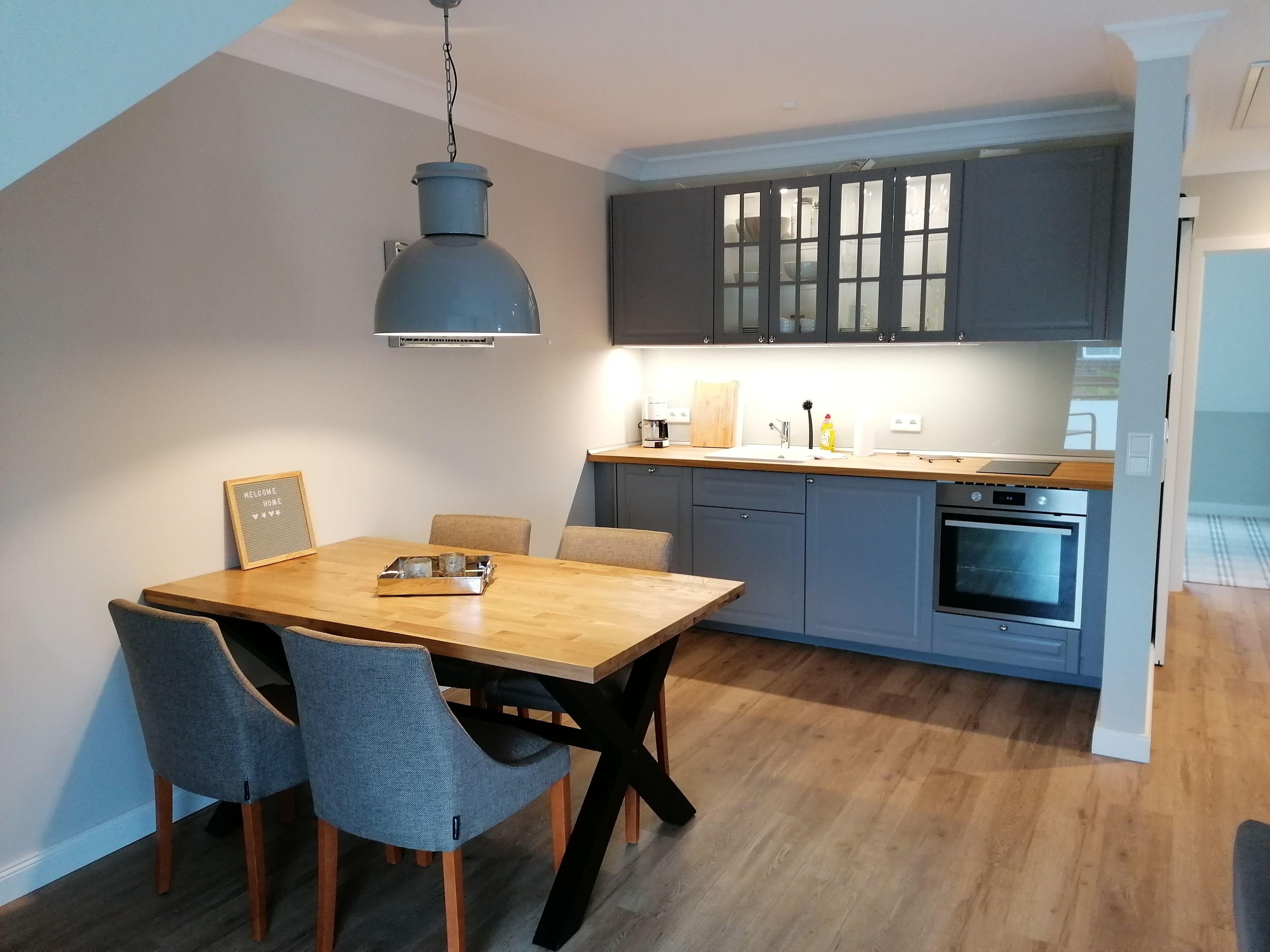 Una cocina moderna con armarios grises, una mesa de comedor de madera y una lámpara colgante.