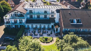 Un edificio grande de varios pisos con un balcón destacado y un patio con mobiliario para exterior.