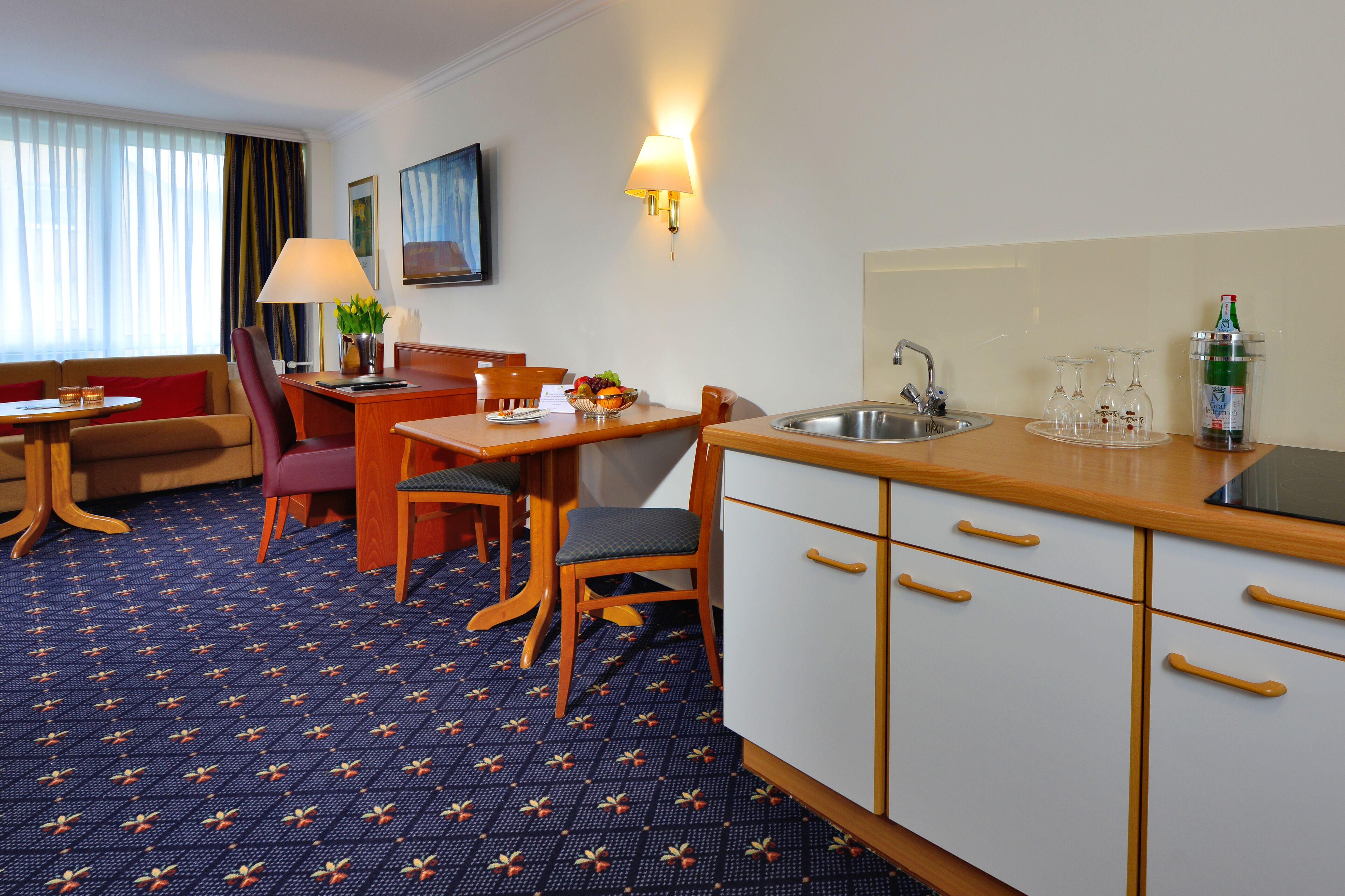 Una habitación de hotel con zona de comedor, kitchenette y espacio de estar con sofá y sillones.