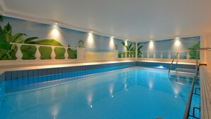Una piscina interior con suelo de baldosas y paredes decoradas con plantas tropicales y un mural de una playa.