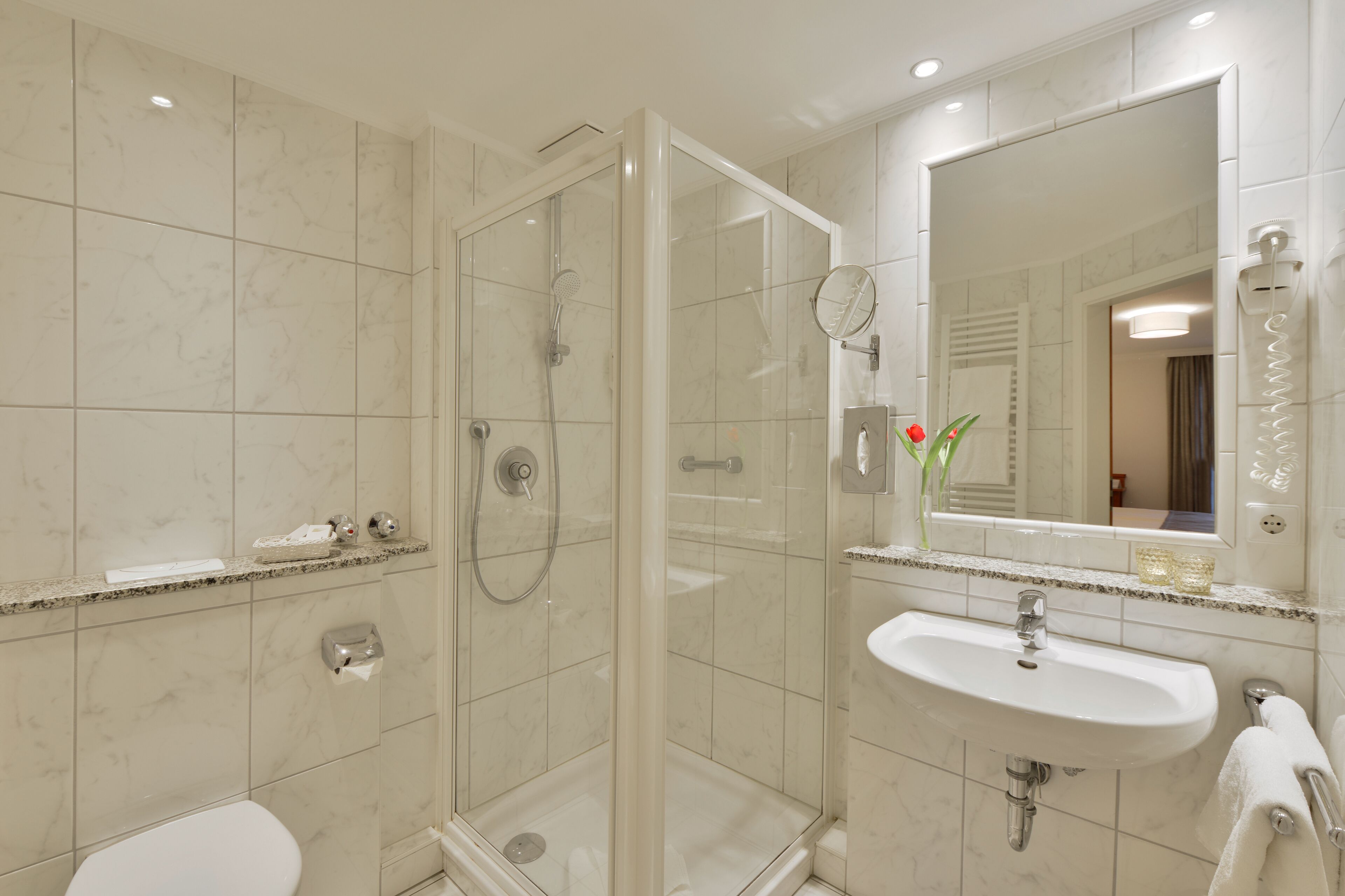 A modern bathroom with a glass-enclosed shower, a white sink, and a large mirror.