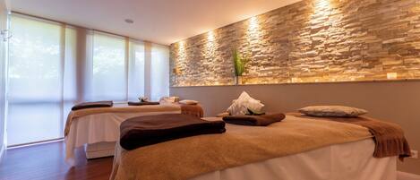 Un cuarto de spa con dos camillas de masaje, una pared de piedra y ventanas amplias.