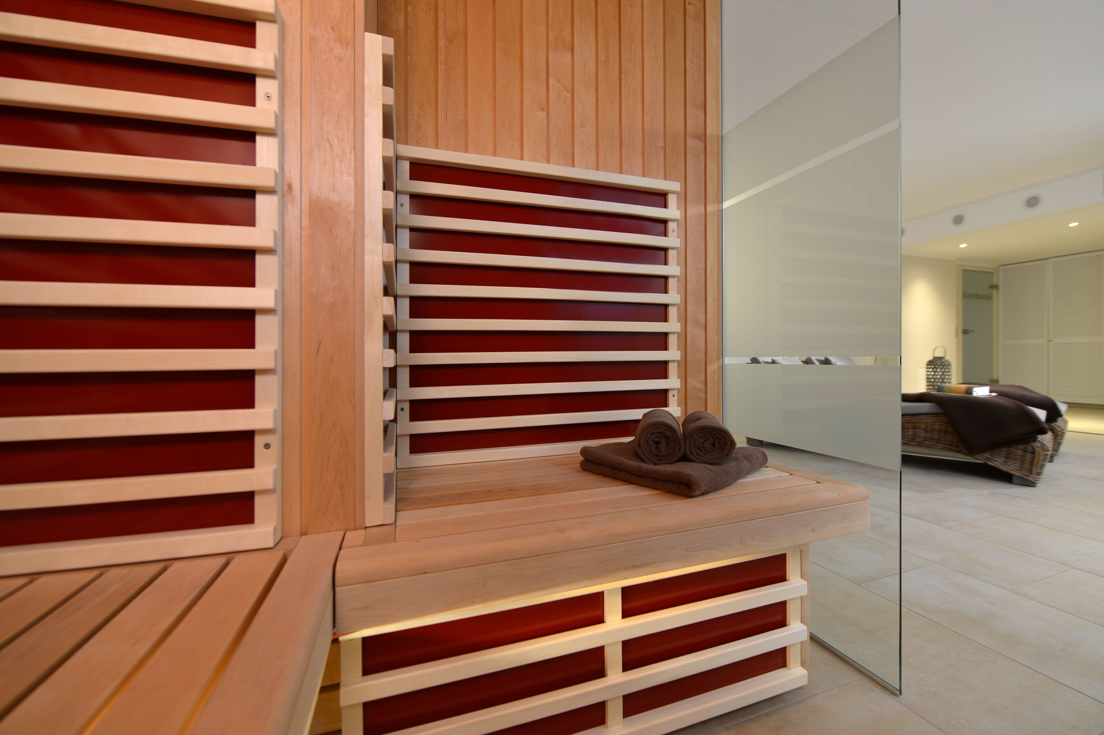 Un área de spa moderna con listones de madera y un banco, un espejo refleja una habitación con una cama y una cesta.