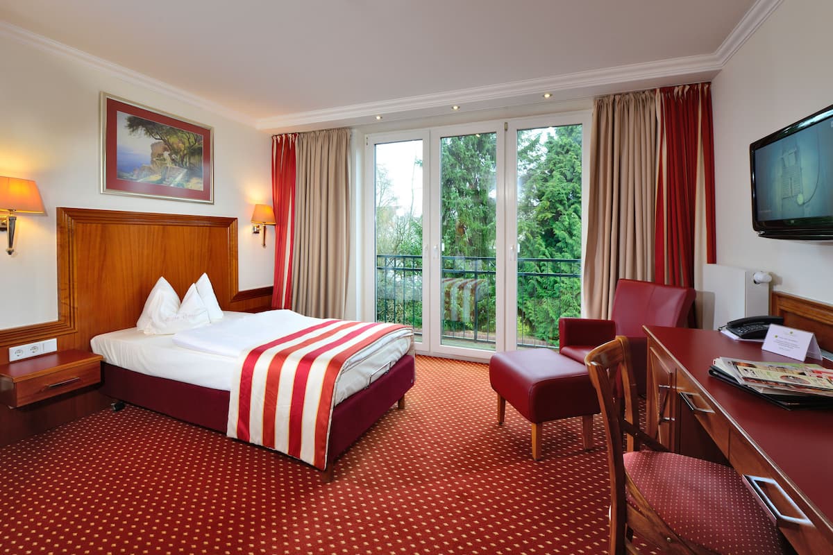 Quarto de hotel com uma cama grande, escrivaninha, cadeira e televisão.