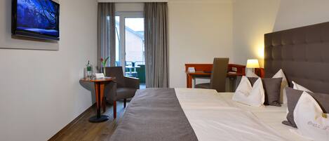 Een hotelkamer met een groot bed, een bureau, een stoel, een aan de muur bevestigde televisie en uitzicht op het landschap door het raam.