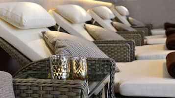 A row of reclining chairs with pillows, a wicker table with glasses, and a wall with a light fixture.
