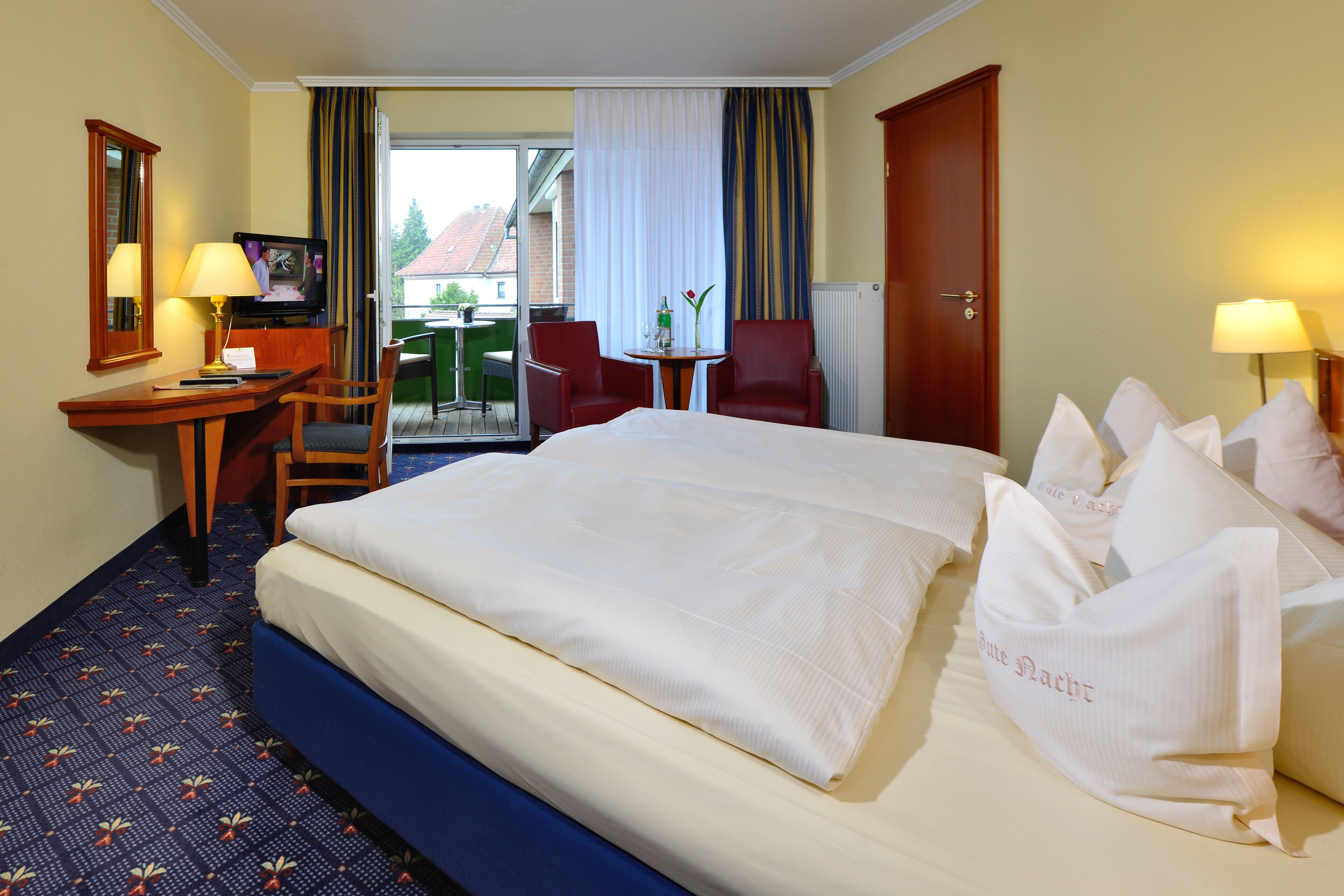 Una habitación de hotel con una cama grande, un escritorio con silla, una mesita y un televisor.